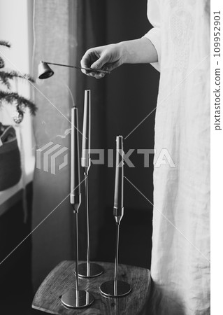 Golden color painted long candles on wooden table at home. Modern living room interior composition with Christmas decorations. New Year, Christmas wallpaper. Black and white photo Golden color painted long candles on wooden table at home. Modern living room interior composition with Christmas decorations. New Year, Christmas wallpaper. Black and white photo 109952901