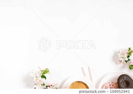 Morning breakfast of a freelance blogger. A cup of coffee with sweet donuts and white apple blossoms in spring on a white background with copy space 109952941