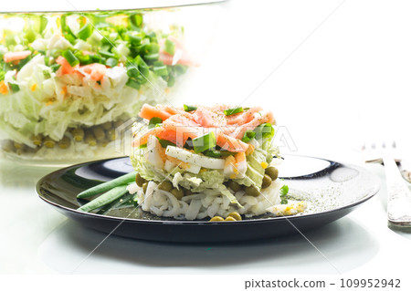 Layered salad of cabbage and other vegetables with pieces of red fish in a plate. 109952942