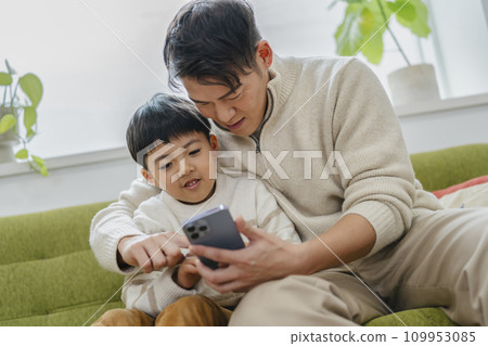 父母和孩子看著智慧型手機螢幕：父親和小學兒子 109953085