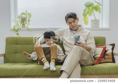 Image of daily life of parent and child: father looking at smartphone and son looking at tablet 109953409