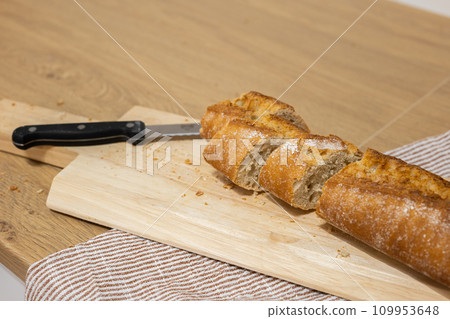 Sliced French bread with knife on cutting board on kitchen towel Sliced French bread with knife on cutting board on kitchen towel 109953648