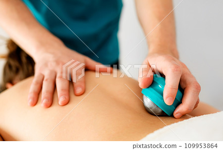 Massage therapist hands doing back massage with special massage accessories Massage therapist hands doing back massage with special massage accessories 109953864
