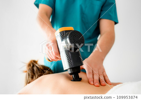 masseuer doing back massage with a vibrating massager for muscles masseuer doing back massage with a vibrating massager for muscles 109953874