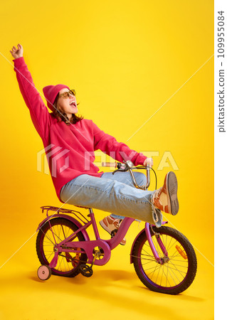 Energetic portrait of girl loudly shouting of joy and happiness because holidays begun riding bicycle against yellow studio background. 109955084