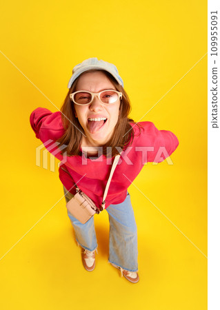 Top view portrait of funny grimacing girl in fashion sunglasses looking at camera against yellow background. Concept of fund and joy. Top view portrait of funny grimacing girl in fashion sunglasses looking at camera against yellow background. Concept of fund and joy. 109955091