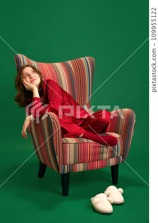 Full length young beautiful girl siting retro chair and dreams of being given gifts from her wish list against green studio background. Full length young beautiful girl siting retro chair and dreams of being given gifts from her wish list against green studio background. 109955122