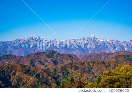Nagano - View of mountains in autumn leaves and snow-covered Mt. Kashima Yarigatake and Mt. Goryu in the Northern Alps from the Ogawa Alps Line. 109956090