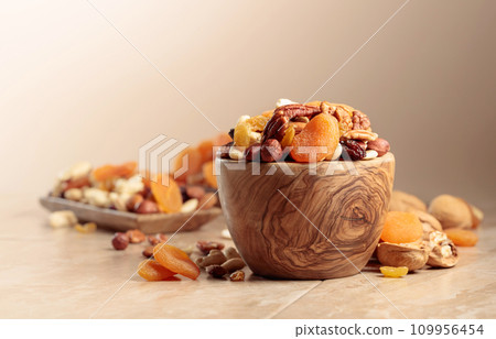 Dried fruits and nuts on a beige ceramic table. 109956454