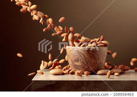 Almond nuts are poured into a wooden bowl. 109956463