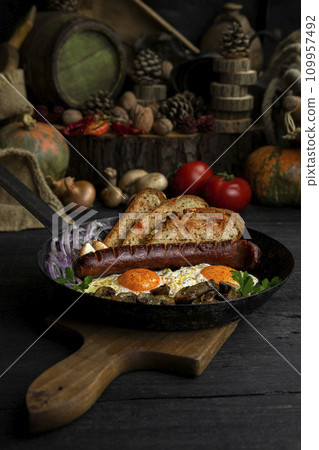 Fried eggs and sausage with mushrooms served in cast iron pan in the kitchen Fried eggs and sausage with mushrooms served in cast iron pan in the kitchen 109957492
