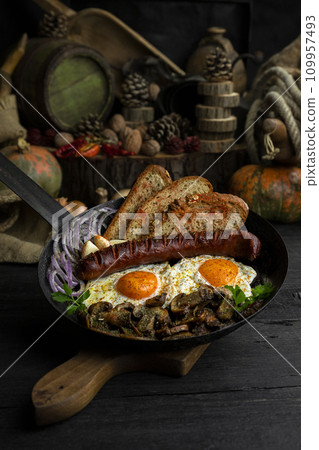 Fried eggs and sausage with mushrooms served in cast iron pan in the kitchen 109957493