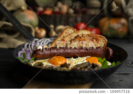Sausage and fried eggs with toasted bread, mushrooms and onions served in cast iron dish. Selective focus on the sausage Sausage and fried eggs with toasted bread, mushrooms and onions served in cast iron dish. Selective focus on the sausage 109957516
