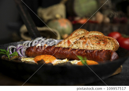 Sausage and fried eggs with toasted bread, mushrooms and onions served in cast iron dish. Selective focus on the sausage Sausage and fried eggs with toasted bread, mushrooms and onions served in cast iron dish. Selective focus on the sausage 109957517