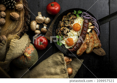 Fried eggs and sausage with mushrooms served in cast iron pan in the kitchen. Top view, flat lay 109957521