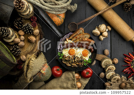 Fried eggs and sausage with mushrooms served in cast iron pan in the kitchen. Top view, flat lay 109957522