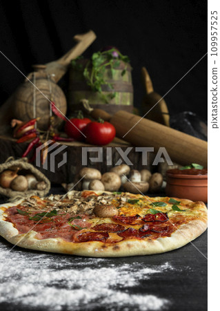Italian Pizza Four Seasons (Pizza Quattro Stagioni) with different ingredients on the wooden table in the kitchen 109957525