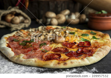 Italian Pizza Four Seasons (Pizza Quattro Stagioni) with different ingredients on the wooden table in the kitchen 109957532