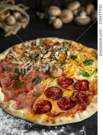 Italian Pizza Four Seasons (Pizza Quattro Stagioni) with different ingredients on the wooden table in the kitchen Italian Pizza Four Seasons (Pizza Quattro Stagioni) with different ingredients on the wooden table in the kitchen 109957592