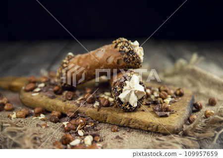 Cannoli, deep fried Italian pastry tubes with a sweet ricotta cheese, chocolate chips and hazelnuts served on a wooden board 109957659