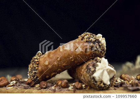 Cannoli, deep fried Italian pastry tubes with a sweet ricotta cheese, chocolate chips and hazelnuts served on a wooden board 109957660