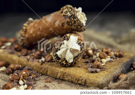 Cannoli, deep fried Italian pastry tubes with a sweet ricotta cheese, chocolate chips and hazelnuts served on a wooden board 109957661