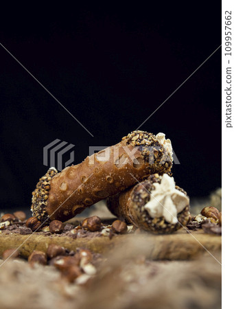Cannoli, deep fried Italian pastry tubes with a sweet ricotta cheese, chocolate chips and hazelnuts served on a wooden board 109957662