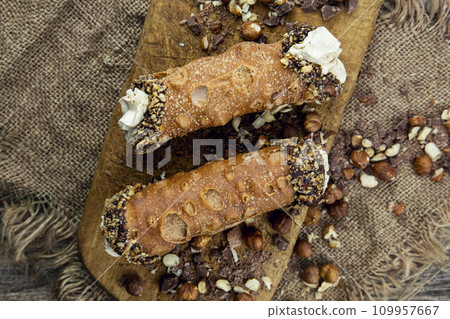 Cannoli, deep fried Italian pastry tubes with a sweet ricotta cheese, chocolate chips and hazelnuts served on a wooden board 109957667
