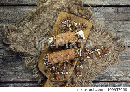 Cannoli, deep fried Italian pastry tubes with a sweet ricotta cheese, chocolate chips and hazelnuts served on a wooden board 109957668