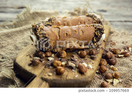 Cannoli, deep fried Italian pastry tubes with a sweet ricotta cheese, chocolate chips and hazelnuts served on a wooden board 109957669