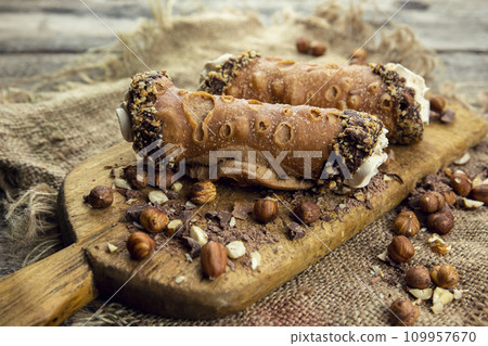 Cannoli, deep fried Italian pastry tubes with a sweet ricotta cheese, chocolate chips and hazelnuts served on a wooden board Cannoli, deep fried Italian pastry tubes with a sweet ricotta cheese, chocolate chips and hazelnuts served on a wooden board 109957670