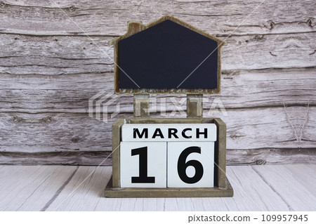 Chalkboard with March 16 date on white cube block on wooden table. 109957945