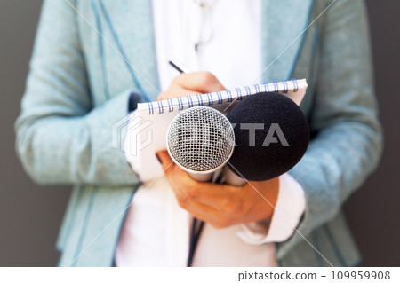 Female journalist at news conference, writing notes, holding microphone Female journalist at news conference, writing notes, holding microphone 109959908