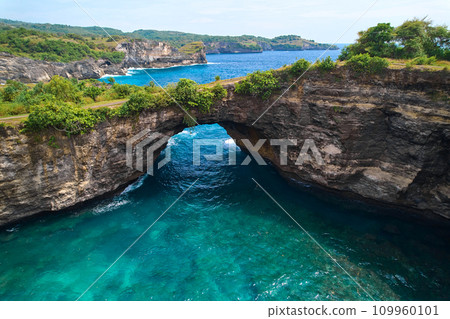 Rock broken by an ocean wave forming an arch in the mountain. Cliff is washed by powerful waves of ocean. Angel's Billabong is a popular tourist destination on the island of Nusa Penida in Indonesia. Rock broken by an ocean wave forming an arch in the mountain. Cliff is washed by powerful waves of ocean. Angel's Billabong is a popular tourist destination on the island of Nusa Penida in Indonesia. 109960101