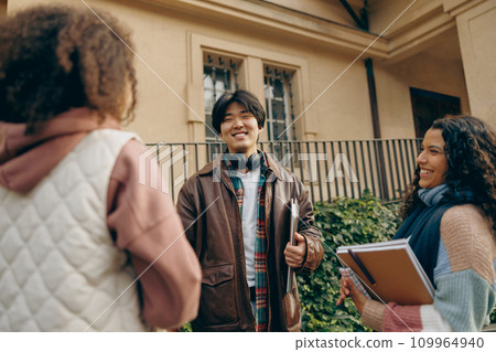 Happy students talking each other standing near university campus and holding books and laptop 109964940