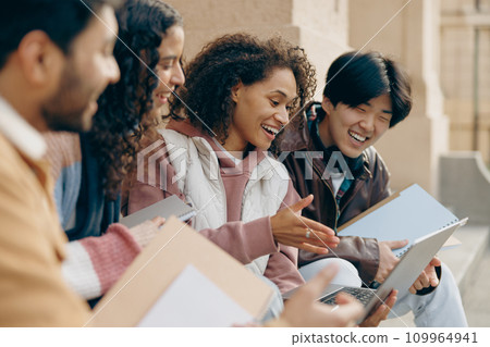 Close up of students sitting on stairs, looking at laptop and discussing their project together 109964941