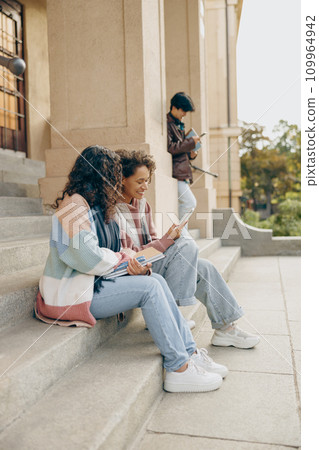 Happy college students having fun using mobile phone together in campus outdoors 109964942