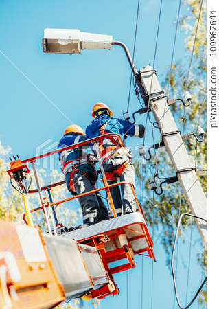 Two professional electricians in hard hats are repairing power lines from cradle of bucket truck Two professional electricians in hard hats are repairing power lines from cradle of bucket truck 109967644