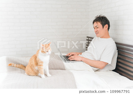A man who telework/remote work with a cat/pet in a bedroom/bedroom at home 109967791