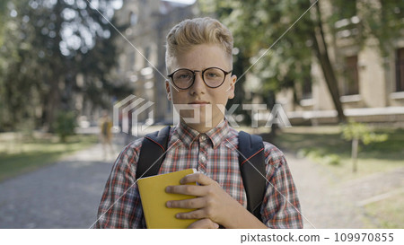 Portrait of shy boy in eyeglasses holding books, first day at new school 109970855