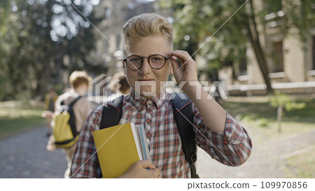 Portrait of smart school boy adjusting eyeglasses and holding books, getting proper education 109970856