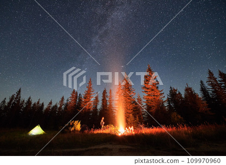 Night camping under starry sky in mountains near forest. Tourists having a rest near campfire under amazing sky full of stars. Camping in Carpathian mountains. Night camping under starry sky in mountains near forest. Tourists having a rest near campfire under amazing sky full of stars. Camping in Carpathian mountains. 109970960