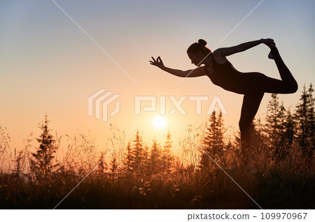 Sporty woman doing lord of the dance pose. Meditation at dawn in mountains. Silhouette of young woman doing yoga asana Natarajasana. Sporty woman doing lord of the dance pose. Meditation at dawn in mountains. Silhouette of young woman doing yoga asana Natarajasana. 109970967