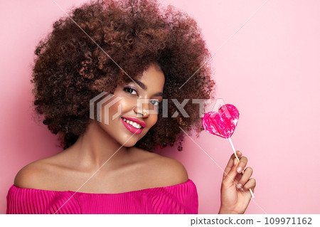 Beautiful portrait of an African girl with a heart shaped lollipop Beautiful portrait of an African girl with a heart shaped lollipop 109971162