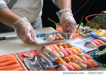 A skilled chef prepare a variety of sushi on a table. Mixing flavor, texture, and color, the chef creates culinary art. Each sushi is a precise masterpiece, showcasing their expertise and dedication. A skilled chef prepare a variety of sushi on a table. Mixing flavor, texture, and color, the chef creates culinary art. Each sushi is a precise masterpiece, showcasing their expertise and dedication. 109971947