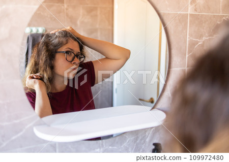 Woman Looking for Gray Hair in the Mirror. Young woman scared of premature aging signs Woman Looking for Gray Hair in the Mirror. Young woman scared of premature aging signs 109972480