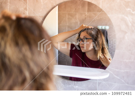 Woman Looking for Gray Hair in the Mirror. Young woman scared of premature aging signs Woman Looking for Gray Hair in the Mirror. Young woman scared of premature aging signs 109972481