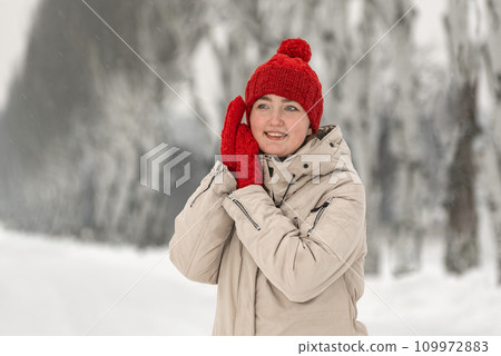 Pretty dancing girl in red hat and mittens on snow background. Young woman in winter clothes in park or forest 109972883