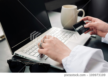 Elegantly poised, a woman's hands gracefully utilize a laptop and credit card for seamless online 109973109