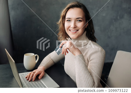 Effortless Online Shopping. Young Woman with Credit Card and Laptop Embraces E-commerce. Young woman Effortless Online Shopping. Young Woman with Credit Card and Laptop Embraces E-commerce. Young woman 109973122